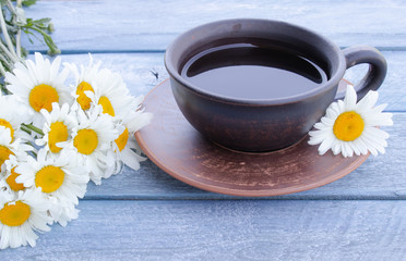 Fototapeta na wymiar Cup of chamomile tea with a bouquet of daisies on a wooden blue background.