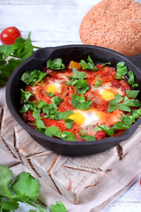 Shakshuka with tomato sauce and quail eggs topped with cilantro in a cast iron pan. Jewish cuisine meal