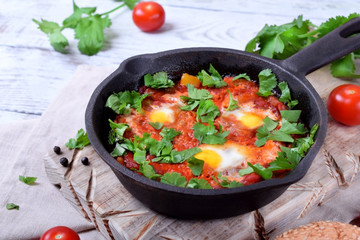 Shakshuka with tomato sauce and quail eggs topped with cilantro in a cast iron pan. Jewish cuisine meal