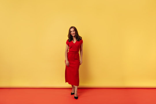 Full-lenght photo charming stylish attractive woman with dark hair wearing red dress  posing over yellow and red background 