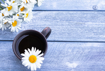 Cup of chamomile tea with a bouquet of daisies on a wooden blue background.