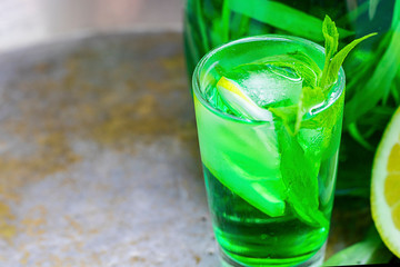 Summer cold green drink with tarragon, mint and lemon in small shot with ice and defocused decanter...