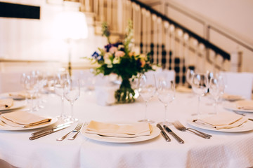 served round table with a white tablecloth and flower arrangement. white plate with a napkin and a glass for wine.