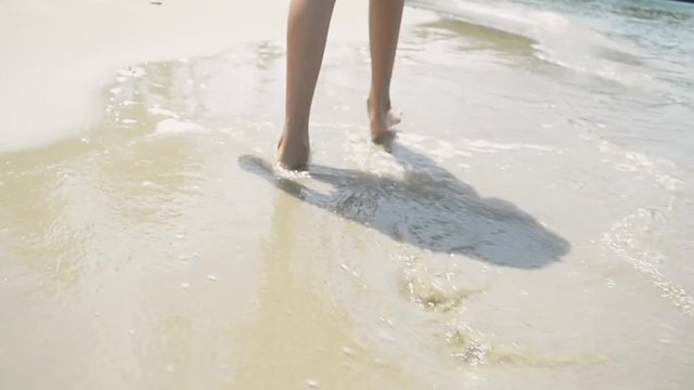Little girl walking bare foot with shallow water on the beach during summer.