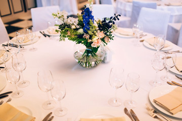 served round table with a white tablecloth and flower arrangement. white plate with a napkin and a glass for wine.