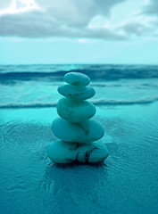 Stack of balanced pebble stones on the beach against splashing waves in blue color