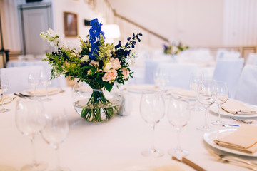 served round table with a white tablecloth and flower arrangement. white plate with a napkin and a glass for wine.