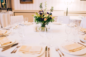served round table with a white tablecloth and flower arrangement. white plate with a napkin and a glass for wine.