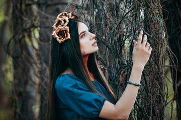 portrait of beautiful brown-haired woman in a long blue dress, with a wreath of golden roses on her head, in the fairy forest, golden paint shimmer on her neck fantasy concept