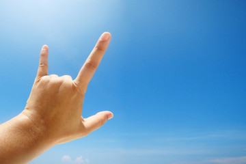 Hand sign of love and showing fingers means I love you on blue sky with sunlight and copty space.