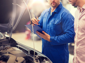 auto service, repair, maintenance and people concept - mechanic with clipboard and man or owner looking at broken car at shop