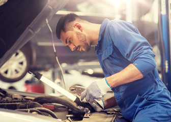 car service, repair, maintenance and people concept - auto mechanic man with lamp working at...