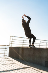 Photo of strong guy 20s doing acrobatics and jumping during morning workout by seaside