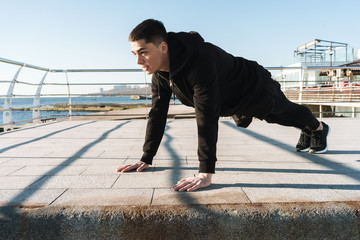 Photo of european guy doing push ups on the floor during morning workout by seaside