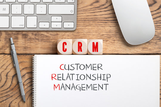 acronym CRM on cubes with a note explaining it as "Customer Relationship Management" on wooden background