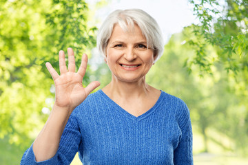 gesture and old people concept - portrait of smiling senior woman in blue sweater showing palm or five fingers over green natural background