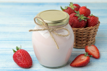 delicious strawberry yogurt in a jar and fresh ripe strawberries on a light blue wooden table.