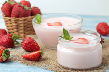 delicious strawberry yogurt in a jar and fresh ripe strawberries on a light blue wooden table.