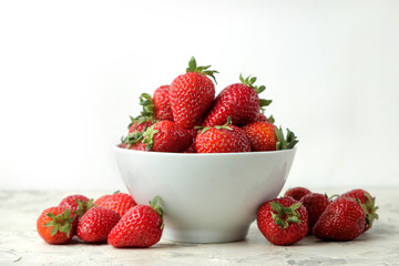 Ripe, delicious strawberries. Red strawberry in a ceramic bowl on a light concrete table.