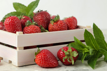 Ripe, delicious strawberries. Red strawberry in a wooden box and mint leaf  on a light concrete...