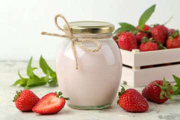 delicious strawberry yogurt in a jar and fresh ripe strawberries on a light concrete table.