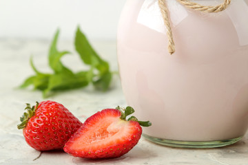 delicious strawberry yogurt in a jar and fresh ripe strawberries on a light concrete table.