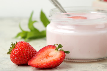 delicious strawberry yogurt in a jar and fresh ripe strawberries on a light concrete table.