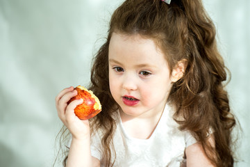 Cute little girl nibbles an apple with pleasure. Sun glare on the face. Emotional portrait of a little beautiful girl holding an apple. Studio 4-5 years.