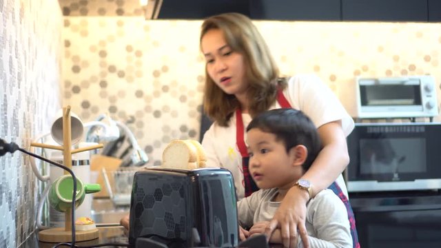 happy Mother teaching son making breakfast toast bread with toaster at home kitchen together . loving family.  child boy excited looking Mom cooking indoors