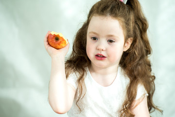 Cute little girl nibbles an apple with pleasure. Sun glare on the face. Emotional portrait of a little beautiful girl holding an apple. Studio 4-5 years.