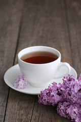 Cup of and lilac flowers on old table