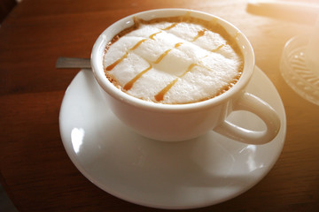 Hot coffee and foam milk in ceramic white cup with sunlight on wooden table. Morning Time