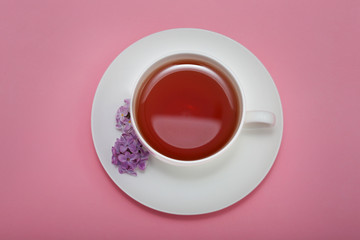 Cup of tea with fresh lilac flowers on pink background