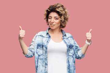 Portrait of happy satisfied young woman with curly hairstyle in casual blue shirt standing, thumbs...