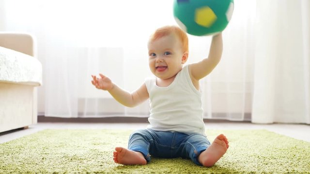 Readhead baby girl playing with a soccer ball on the floor in sunny room