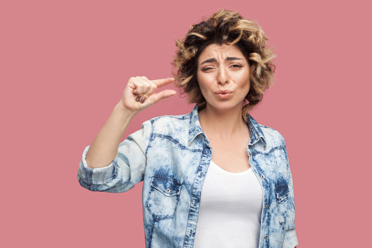 Give me a few more. Portrait of pleased worry young woman with curly hairstyle in casual blue shirt standing and showing a few gesture and pleading. indoor studio shot, isolated on pink background.