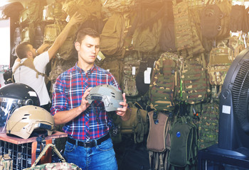 Young guys choosing helmet in military shop