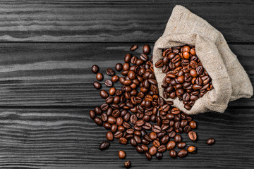 Coffee beans in coffee burlap bag on wooden surface.
