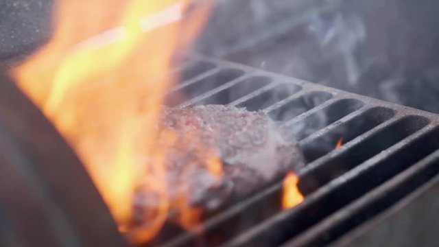 Cooking hamburger. Beef or pork cutlet grilling on grid. Cook man preparing a burger patty on the grill. Laid on the grill and overturned flatware. Family summer vacation. Slow motion.