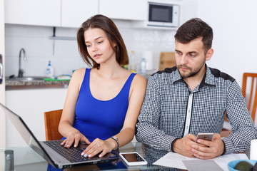 Obraz premium Young woman working at laptop and boyfriend using phone at home