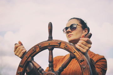 The girl controls the yacht, hands on the steering wheel,  handwheel on sky background