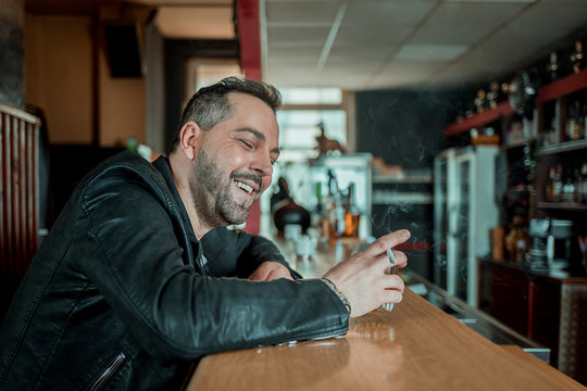 Laughing man in a bar at the counter with a whiskey and a cigarette in his hand