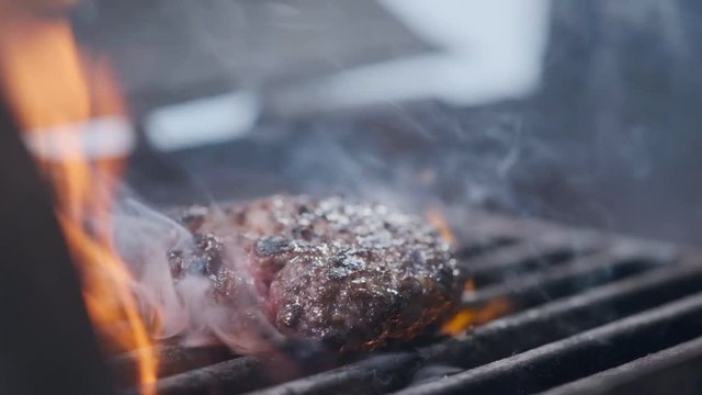 Cooking hamburger. Beef or pork cutlet grilling on grid. Cook man preparing a burger patty on the grill. Laid on the grill and overturned flatware. Family summer vacation. Slow motion.