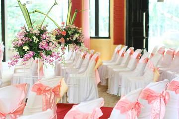 Beautiful chairs decoration with pink ribbon and Bouquet of orchids with flowers in a vase in wedding event hall.
