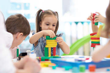 Little children build wooden toys at home or daycare. Emotional kids playing with color blocks....