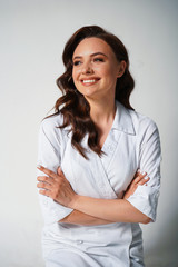 Happy beautiful young female doctor in white medical jacket isolated on white background. Brunette woman cosmetologist. Cross hands. Medical concept. Healthcare