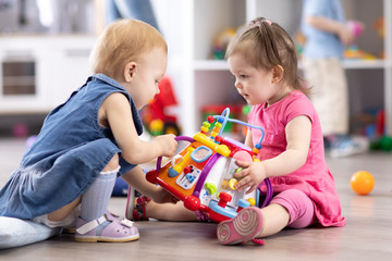 Babies conflict in nursery. Child girl trying to take away toy from another kid.
