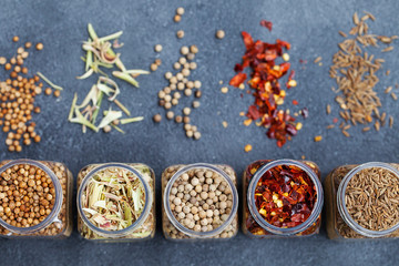 Assortments of spices in jars on grey stone background. Top view. Copy space.