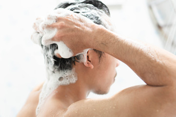 Closeup young man washing hair with with shampoo in the bathroom, health care concept, selective focus - obrazy, fototapety, plakaty