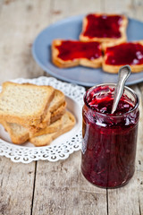 Homemade cherry jam and fresh toasted cereal bread slices plates closeup on rustic wooden table background.